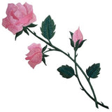 Detailed embroidered patch depicting a rose stem with two open pink blossoms and one closed pink bud. The flowers have a shimmering or iridescent quality, and the leaves and stems are dark green.