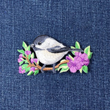 Embroidered patch of a chickadee bird on a branch with flowers on denim fabric