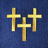 Three gold cross patches on a blue fabric background