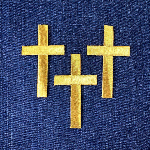 Three gold cross patches on a blue fabric background