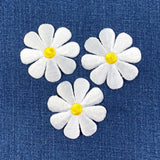 Three white daisy flower patches with yellow centers on a blue denim background