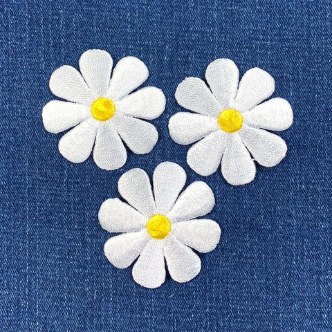 Three white daisy flower patches with yellow centers on a blue denim background