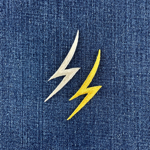 Two lightning bolt patches, one silver and one gold, on a blue denim background.