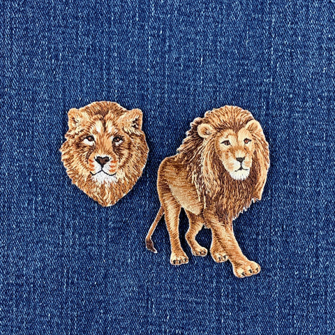 Two lion-themed patches, one lion head and one full lion, displayed on a blue denim fabric background.