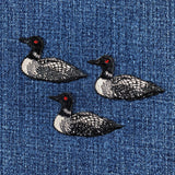 Three embroidered loon bird patches on a denim fabric background