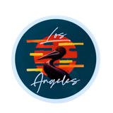 Circular sticker with a dark teal background. The design features a stylized brown pelican silhouette centered over an orange-red circle resembling a sunset, with horizontal yellow and orange stripes. White cursive text above and below the pelican reads "Los Angeles."