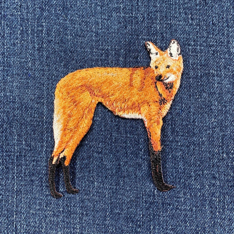 Embroidered maned wolf patch with a black and orange color scheme, designed for iron on application, on a denim fabric background