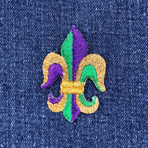 Fleur-de-lis patch on denim fabric with purple, green, and gold colors.