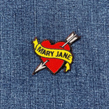 a heart shaped patch with an arrow through it with the words 'MARY JANE' in the center, displayed on a denim background