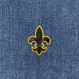 A black and metallic gold embroidered fleur de lis patch with an iron on application on a denim background