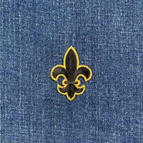A black and metallic gold embroidered fleur de lis patch with an iron on application on a denim background