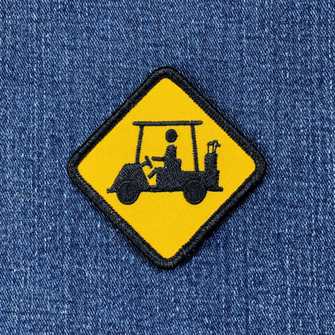 Embroidered patch of a yellow diamond traffic sign with a black silhouette of a golf cart on blue denim fabric.