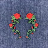 Two embroidered rose stem patches with red roses and green leaves, placed on a blue denim fabric background.