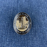A black, silver, and beige medallion with Mesa Verde National Park text and an illustration of a ruin displayed on a denim background