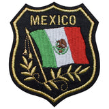 An embroidered shield-shaped patch featuring the word 'MEXICO' in gold above a Mexican flag with a gold laurel wreath on a black background.