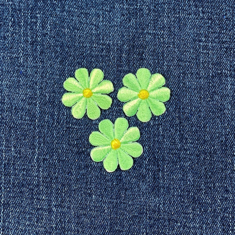 Three green floral patches with yellow centers on a blue denim background