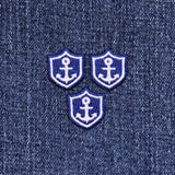 Three embroidered patches featuring a mini anchor design on a blue and white nautical shield on a denim background