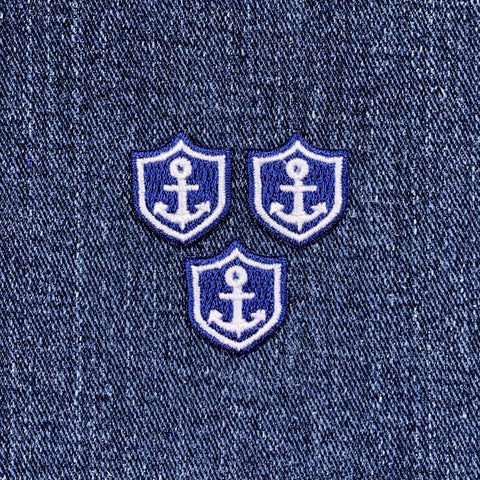 Three embroidered patches featuring a mini anchor design on a blue and white nautical shield on a denim background