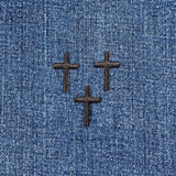 Three black cross applique patches with an embroidered design, intended for iron-on application, on a denim background
