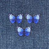Three blue butterfly patches on a denim background
