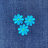 Three blue flower patches with green centers on a denim background