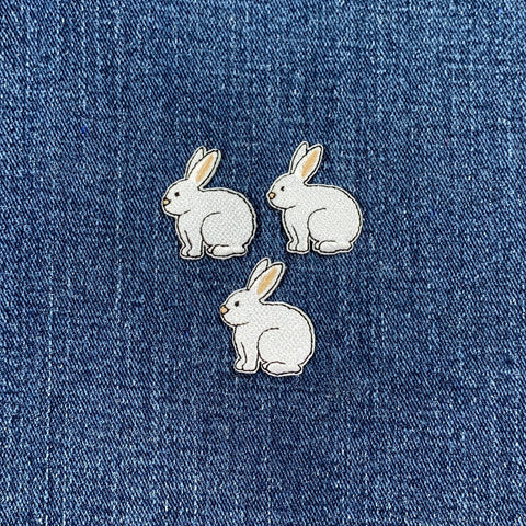 Three white rabbit patches on a blue denim background