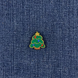 A small embroidered Christmas tree patch with green needles, colorful ornaments, and a gold star, shown on a dark blue denim fabric background.