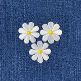 Three white daisy flower patches with yellow centers on a denim background