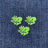 Three miniature green frog applique patches on a denim background
