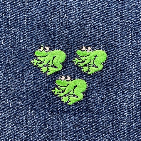 Three miniature green frog applique patches on a denim background