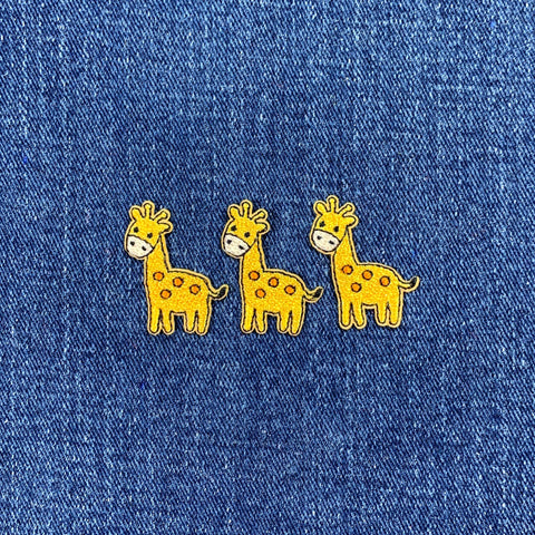 Three miniature giraffe patches on a blue denim background