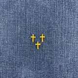 Three small gold cross-shaped patches arranged in a triangle on a blue denim fabric background.