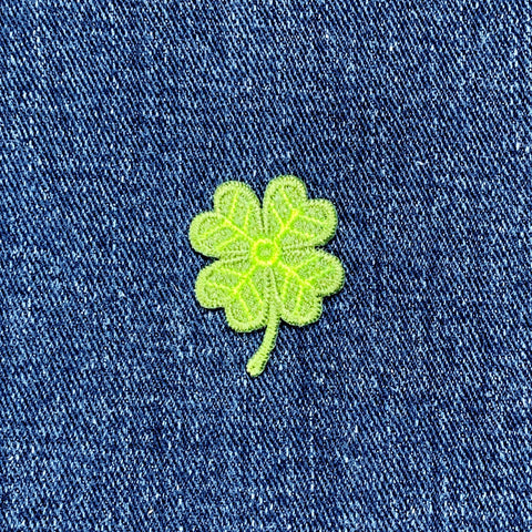 Green four-leaf clover patch on blue denim fabric