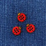 Three red and black ladybug patches on blue denim fabric