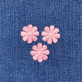Three pink flower patches with white centers on a blue denim background