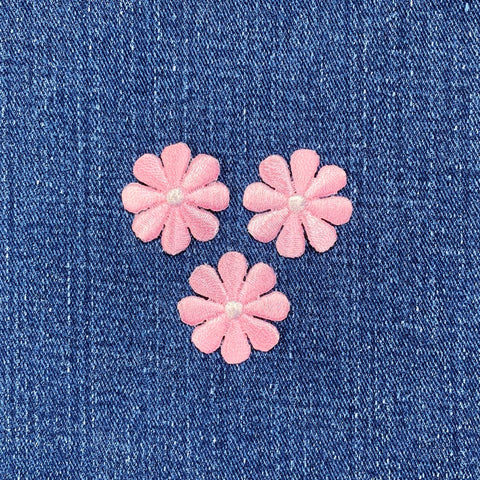 Three pink flower patches with white centers on a blue denim background