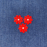 Three red flower patches with white centers on a blue denim background