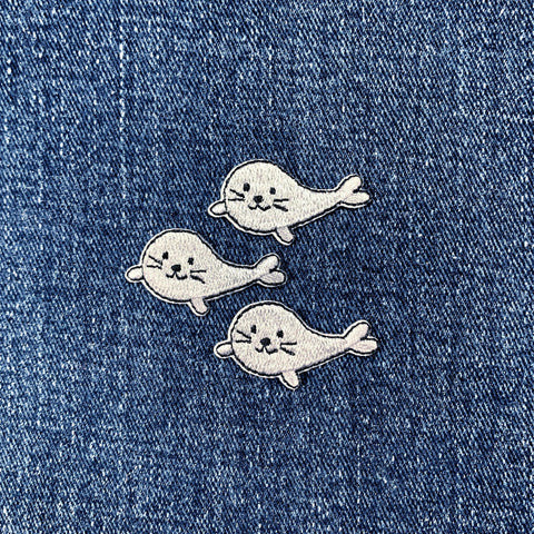 Three cartoon seal patches on a denim background