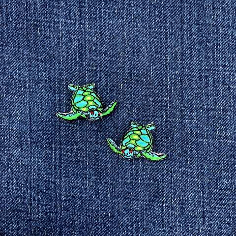 Two green turtle-shaped patches on a blue denim background