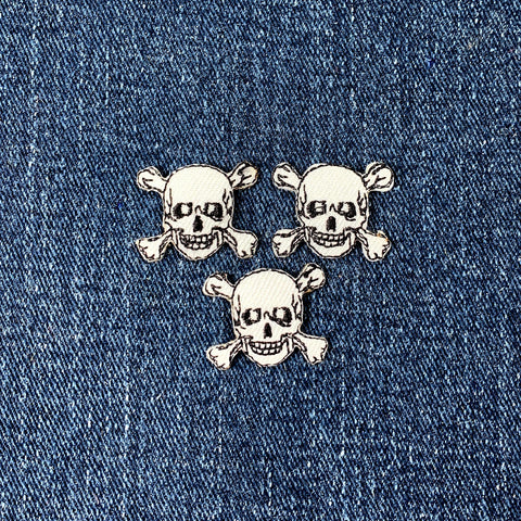 Three skull and crossbones patches on a denim background