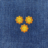 Three sun-shaped smiley face patches on a denim background