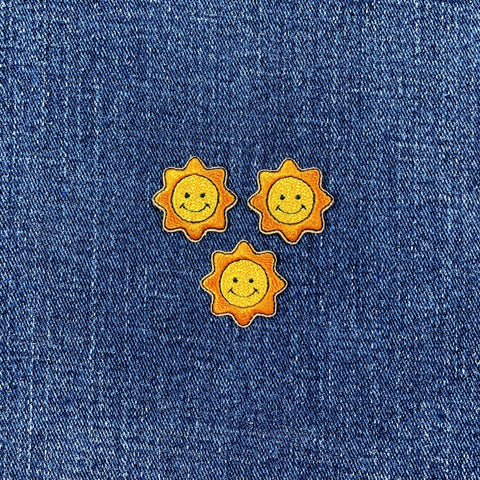 Three sun-shaped smiley face patches on a denim background