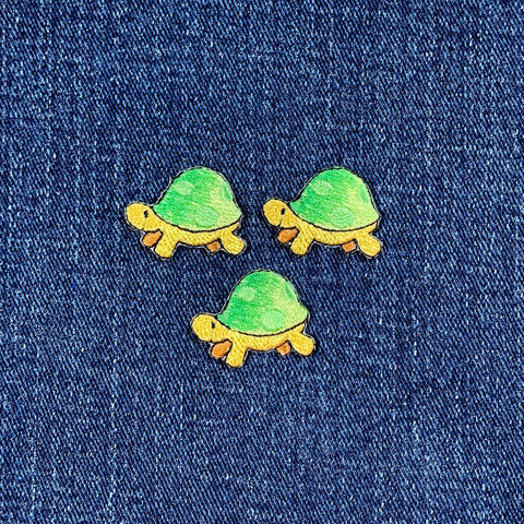 Three green turtle patches on a denim background