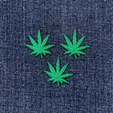 Three green cannabis leaf patches on a denim background