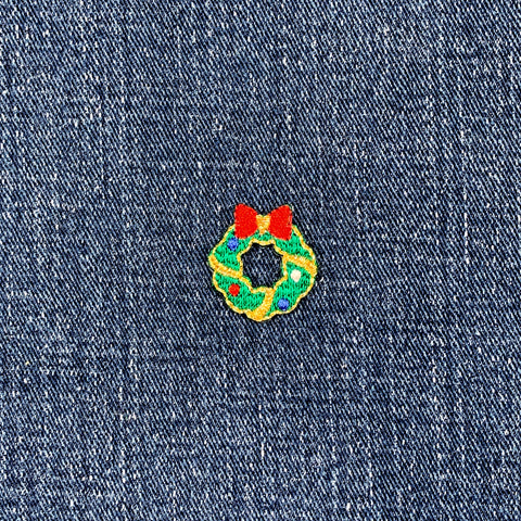 Embroidered Christmas wreath patch with red bow on denim fabric