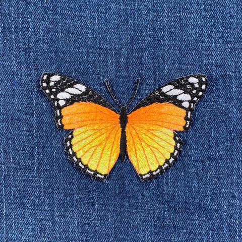 Butterfly patch with orange and black wings on blue denim fabric