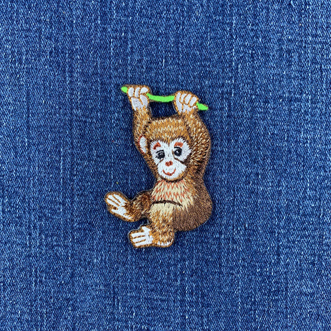 embroidered monkey hanging on a vine patch displayed on a denim background