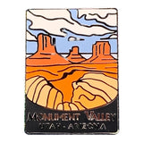 A rectangular enamel pin featuring a stylized Monument Valley landscape with orange rock formations, beige dunes, blue sky, and white clouds. The bottom reads 'MONUMENT VALLEY UTAH - ARIZONA' on a black background.
