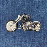 An embroidered patch of a black and silver chopper motorcycle, shown on a blue denim fabric background.