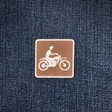 Denim fabric with a brown patch featuring a white motorcycle and rider design.